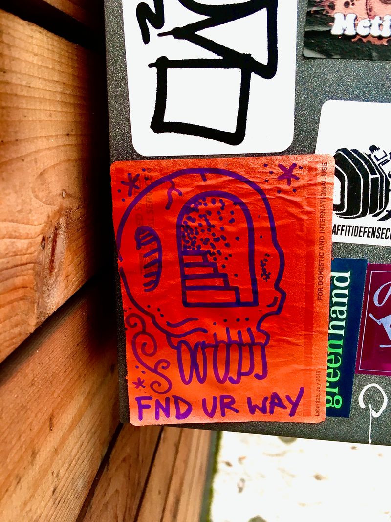 A hand-drawn sticker on a road sign that says 'FND UR WAY' under a skull with a staircase leading into the brain compartment.