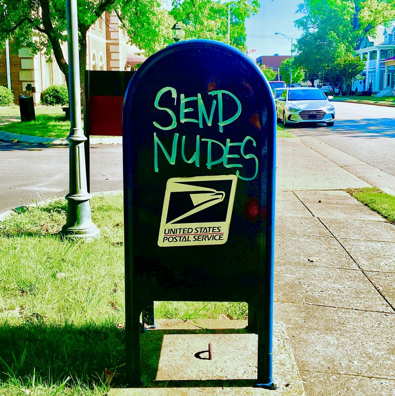 A quintessential United States Postal Service® mailbox with 'SEND NUDES' painted on the side, right above the logo.
