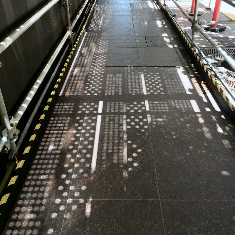 Construction-filtered sunlight projecting a binary pattern on the sidewalk.